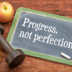 Image of blackboard with dumbells and apple. Written on the blackboard is "progress, not perfection"