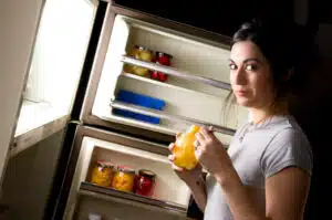 women snacking with fridge door open at night - it is dark