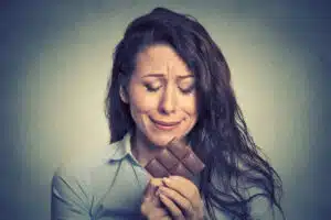 woman looking upset and eating chocolate - pcos cravings