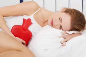 woman lying down with a red hot water bottle on her stomach to help with period pain