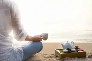 Woman meditating and drinking tea on beach